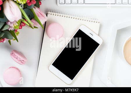 Lady blogger Schreibtisch mit rosa Blüten und Macaron Kuchen auf weißem Hintergrund, weiblich Home Office workspce mit Kaffee und Smartphone Mock-u Stockfoto