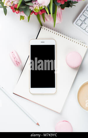 Lady blogger Schreibtisch mit rosa Blüten und Macaron Kuchen auf weißem Hintergrund, weiblich Home Office workspce mit Kaffee und Smartphone Mock-u Stockfoto
