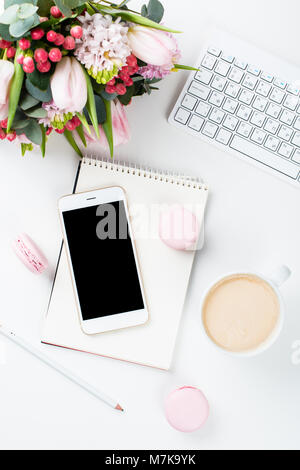 Lady blogger Schreibtisch mit rosa Blüten und Macaron Kuchen auf weißem Hintergrund, weiblich Home Office workspce mit Kaffee und Smartphone Mock-u Stockfoto