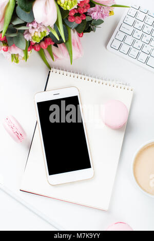 Lady blogger Schreibtisch mit rosa Blüten und Macaron Kuchen auf weißem Hintergrund, weiblich Home Office workspce mit Kaffee und Smartphone Mock-u Stockfoto