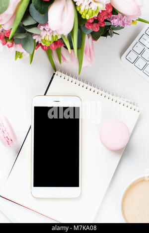 Lady blogger Schreibtisch mit rosa Blüten und Macaron Kuchen auf weißem Hintergrund, weiblich Home Office workspce mit Kaffee und Smartphone Mock-u Stockfoto