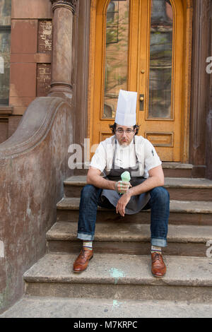 Ein Chef sitzen auf New York City stoop essen ein Eis Kegel. Stockfoto