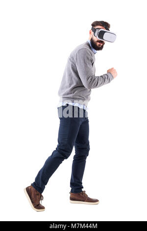 Seitenansicht der junge Bartgeier Smart Casual Mann mit VR-Brille läuft erstaunt und Kamera. Voller Körper auf weißem Hintergrund. Stockfoto
