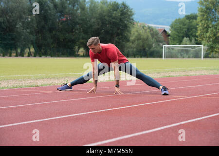 Junge Athlet Mann Entspannen und Strech Bereit für Laufen bei Leichtathletik Rennstrecke auf Stadium Stockfoto