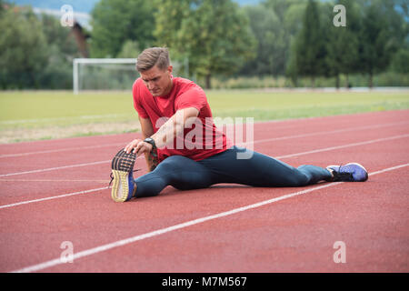 Junge Athlet Mann Entspannen und Strech Bereit für Laufen bei Leichtathletik Rennstrecke auf Stadium Stockfoto