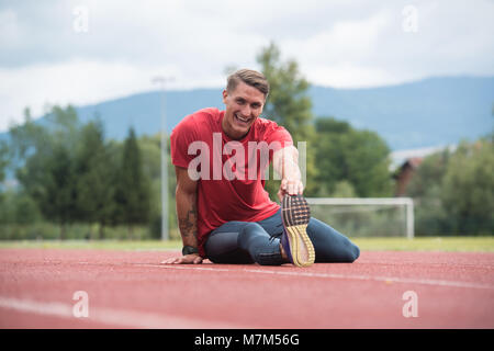 Junge Athlet Mann Entspannen und Strech Bereit für Laufen bei Leichtathletik Rennstrecke auf Stadium Stockfoto