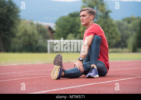 Junge Athlet Mann Entspannen und Strech Bereit für Laufen bei Leichtathletik Rennstrecke auf Stadium Stockfoto