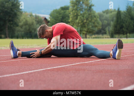 Junge Athlet Mann Entspannen und Strech Bereit für Laufen bei Leichtathletik Rennstrecke auf Stadium Stockfoto