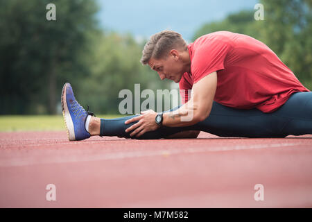 Junge Athlet Mann Entspannen und Strech Bereit für Laufen bei Leichtathletik Rennstrecke auf Stadium Stockfoto