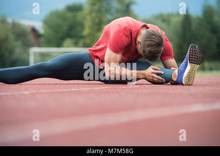 Junge Athlet Mann Entspannen und Strech Bereit für Laufen bei Leichtathletik Rennstrecke auf Stadium Stockfoto