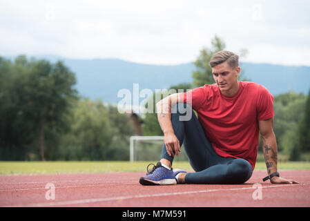 Junge Athlet Mann Entspannen und Strech Bereit für Laufen bei Leichtathletik Rennstrecke auf Stadium Stockfoto