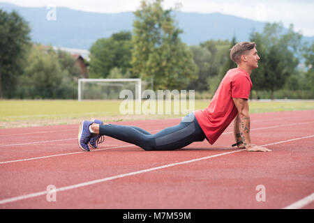 Junge Athlet Mann Entspannen und Strech Bereit für Laufen bei Leichtathletik Rennstrecke auf Stadium Stockfoto