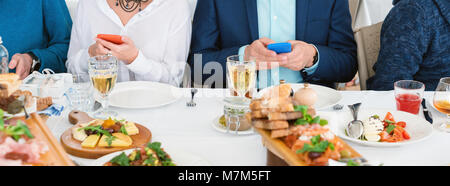 Freunde im Cafe sitzen, essen und trinken Alkohol, während Sie ein Handy benutzen. Fokus auf Telefon, kein Gesicht Stockfoto