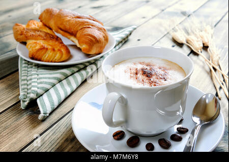 Nahaufnahme einer Tasse Kaffee mit Milch, Croissants und Brioche auf einem antiken Holztisch. Stockfoto