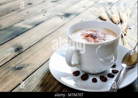 Nahaufnahme von einer Tasse Kaffee mit Milch auf einem antiken Holztisch. Stockfoto
