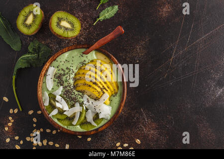 Grünkohl vegan Smoothie Schüssel mit Kokosnuss, Chia, Apple und Kiwi. Gesunde vegane Ernährung Konzept. Dunkle Rusty Hintergrund, Ansicht von oben Stockfoto