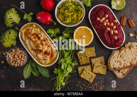 Veganes essen Hintergrund. Vegetarische Snacks: hummus Hummus, rote Beete, Erbsen dip, Gemüse, Tofu. Ansicht von oben, dunklen Hintergrund, kopieren. Stockfoto