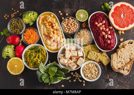 Veganes essen Hintergrund. Vegetarische Snacks: hummus Hummus, rote Beete, Erbsen dip, Gemüse, Tofu. Ansicht von oben, dunklen Hintergrund, kopieren. Stockfoto