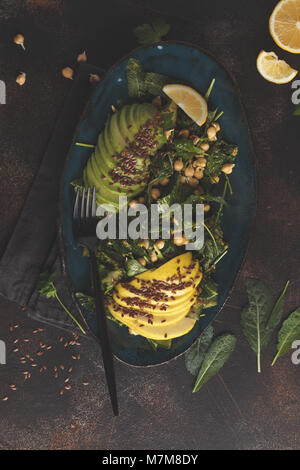 Gesund vegan Avocado, Kichererbsen, kale Salat in einem Vintage blauen Platte auf einem dunklen Hintergrund rostig. Veganes essen Konzept. Stockfoto