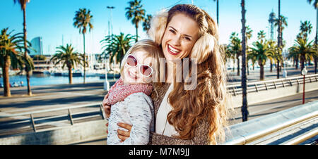 In Barcelona für einen perfekten Winter. Happy trendy Mutter und Kind Touristen am Bahndamm in Barcelona, Spanien Stockfoto