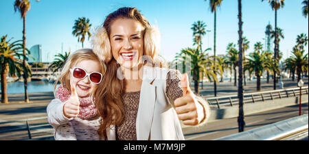 In Barcelona für einen perfekten Winter. Glückliche junge Mutter und Kind Touristen in Barcelona, Spanien, Daumen hoch Stockfoto