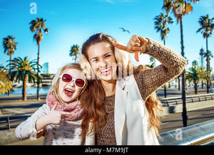 in Barcelona für einen perfekten Winter. Porträt des Lächelns moderne Mutter und Kind Touristen am Ufer in Barcelona, Spanien-Rahmung mit Händen Stockfoto