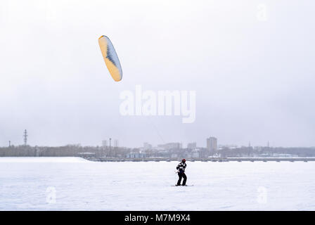 Snowkiter gleitet auf dem Eis eines zugefrorenen Fluss vor dem Hintergrund des Stadtbildes Stockfoto