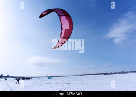 Snowkiter gleitet auf dem Eis eines zugefrorenen Fluss vor dem Hintergrund des Stadtbildes Stockfoto