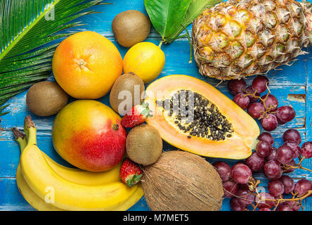 Reif saftig Tropischer Sommer saisonale Früchte Mango Papaya Ananas Kokos Kiwi, Bananen, Erdbeeren, Weintrauben, Zitrusfrüchte auf großen Palm Leaf auf Blau Holz zurück Stockfoto