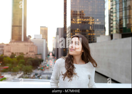 Schöne junge Frau sitzt auf einer Brücke über den Boulevard in der städtischen Landschaft, Downtown, bei Sonnenuntergang, auf der Suche Seite.