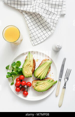 Avocado Toast und Orangensaft auf weißem Hintergrund, Ansicht von oben. Konzept der gesunden Frühstück, gesund leben, Diät, Fitness, Gewichtsreduktion, vegan, Stockfoto
