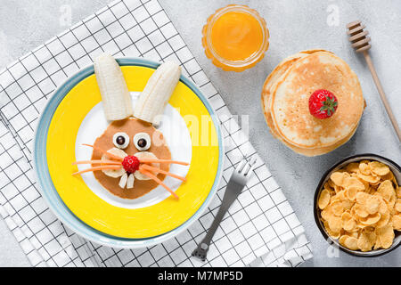 Frühstück für Kinder. Osterhase Pfannkuchen, Honig und Cornflakes. Ansicht von oben. Konzept der Osterferien, gesundes Frühstück für Kinder, Kinder Essen Stockfoto