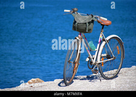 Altes Fahrrad steht an einem sonnigen Tag auf einem Pier mit Meer im Hintergrund. Stockfoto