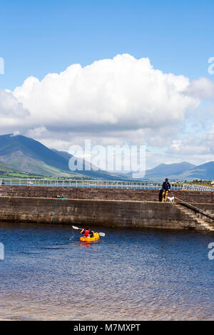 Mann, der seinen Hund am Ende der Pier, Hafenmauer, orange Kanu, vor einer atemberaubenden Landschaft Hintergrund, Ring of Kerry Kerry Irland Stockfoto