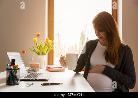 Happy preganant Frau auf ihren Bauch während der Arbeit eine Pause von der Arbeit. Wohlbefinden am Arbeitsplatz schwanger Stockfoto
