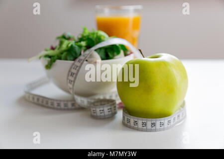 Maßband um den Apfel, Schüssel grünem Salat und ein Glas Saft. Gewicht Verlust und richtige Ernährung Konzept Stockfoto
