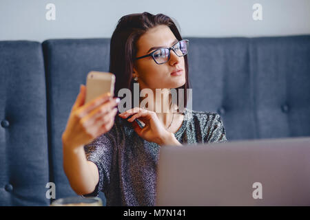 Ein charmantes Mädchen in einer Brille für einen Laptop eine selfie in einem Cafe Stockfoto