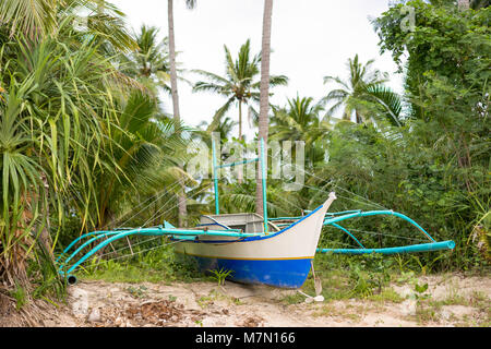 Eine traditionelle philippinische Fischerboot mit stabilisierenden Ausleger auf eine bewachsene Sandbank geparkt gerade weg von einem tropischen weißen Sandstrand. Stockfoto