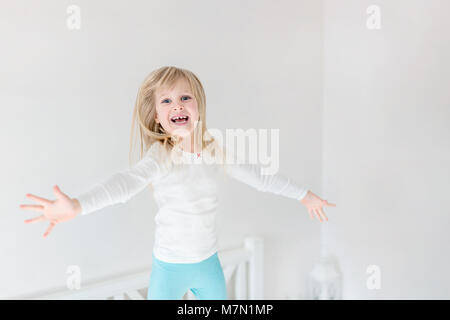 Glückliches Kind über dem Bett springen. Süße kleine blonde Mädchen Spaß haben im Innenbereich. Glücklichen und sorglosen Kindheit Konzept Stockfoto