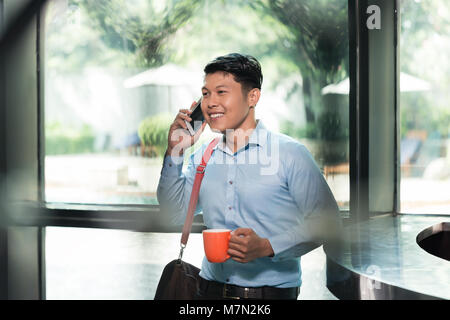 Freundliche Asiatische junge Mann Gespräch am Handy während einer Tasse Kaffee Holding Stockfoto