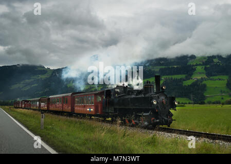 Retro Lokomotive mit Rauchen Motor vorwärts zu bewegen, in den Alpen. Malerischer Blick auf vintage Trainieren gegen Wald und schönen Hügeln in Europa. Stockfoto