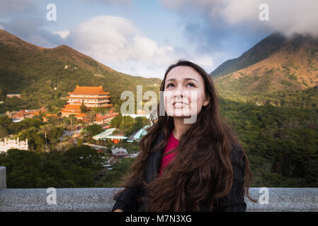 Trendy Frau steht auf Observation Deck, und sieht mit Interesse. Junge Frau, die auf dem Hintergrund der Berge und Bauen in China Stil Stockfoto