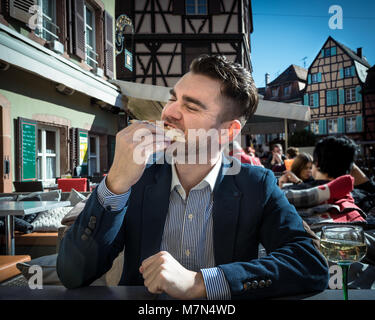 Sehr hungrig Mensch isst Pizza im Cafe im Freien. Junger Mann im Anzug ist Essen Mahlzeit mit Wein. Terrasse mit schöner Aussicht auf vintage Gebäude in Europa Stockfoto
