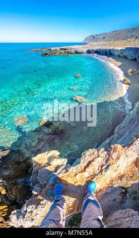 Vertorama eines Mannes stehen am Rand der Klippe oberhalb der wunderschönen Strand in Milatos, Kreta, Griechenland. Stockfoto