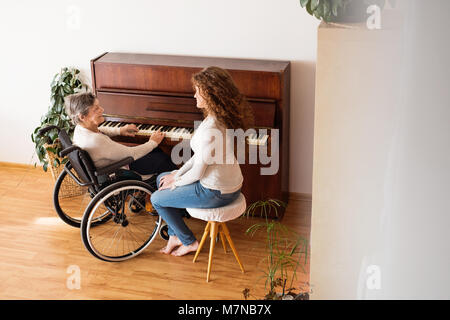 Ein Mädchen mit Großmutter im Rollstuhl Klavier spielen. Stockfoto