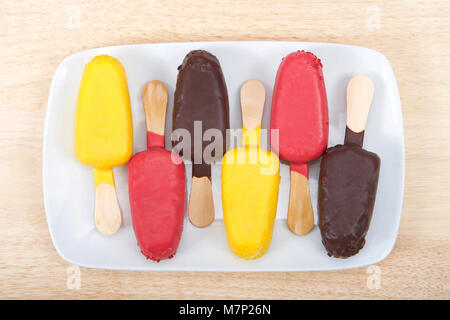 Bunten Süßigkeiten, Kuchen Eis am Stiel auf einem weißen Teller wechselnder Aromen und die Richtung der Kuchen Pops, Festlegung auf hellem Holz Tisch. Fun Geburtstag teil Stockfoto