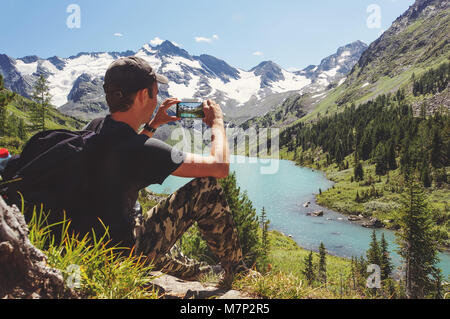 Touristische in schwarzen T-Shirt nimmt Fotos mit Smart Phone auf der Spitze des Felsens. Verträumte Hügellandschaft unten. Die schöne Landschaft des Altaigebirges. Stockfoto