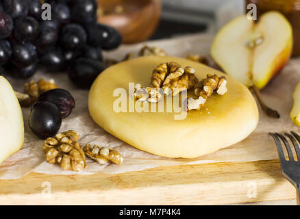 Käse, Honig, Trauben, Birnen und Nüsse auf Holzbrett Stockfoto