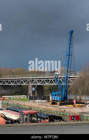 Bootswerft mit drohenden Gewitterwolken mit mehreren farbigen Kähne und hellen blauen Kran- und Eisenbahnbrücke über den Kanal im Hintergrund Stockfoto