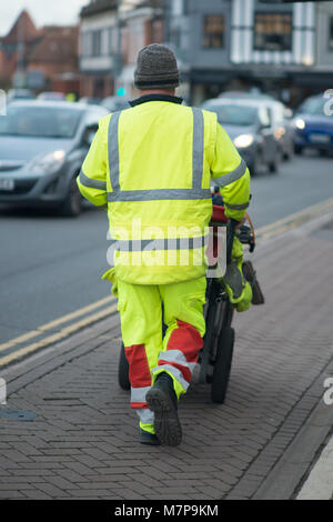 Street Sweeper geht weg drücken Ref und grau Barrow mit dem Gebäude im Hintergrund Stockfoto